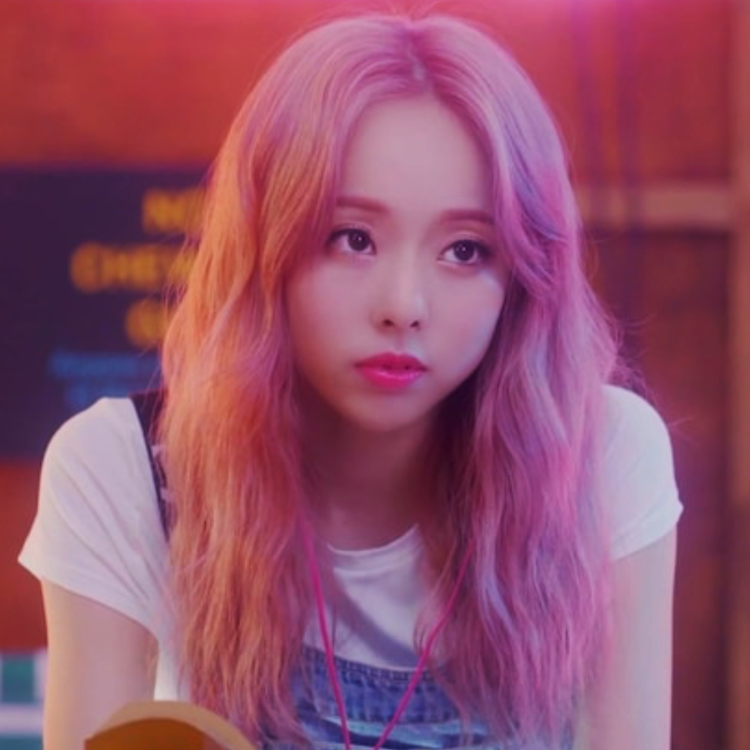 Vivi from the 'Everyday I Love You' music video. She has long light pink hair and is wearing blue overalls. She is holding a book and looking up.